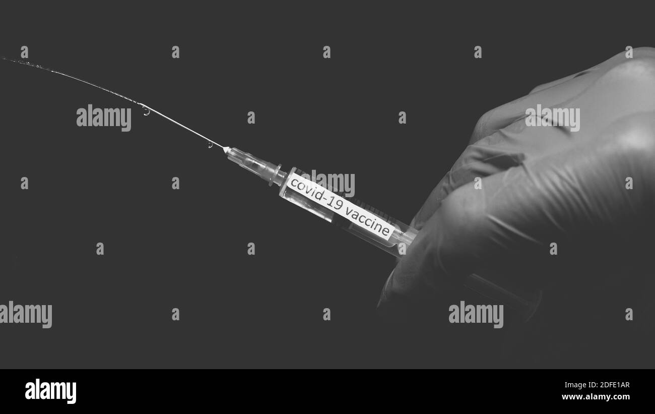 Presser le vaccin du coronavirus hors d'une seringue, peinture noire et blanche avec un traitement pour le covid-19, gros plan. Banque D'Images