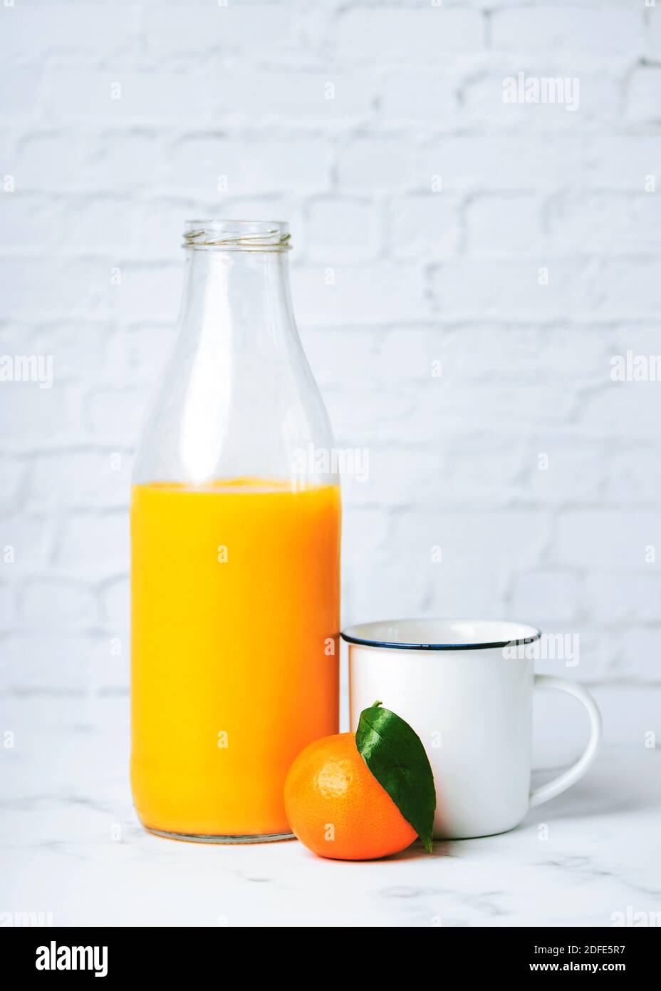 Jus d'orange frais et sain dans une bouteille de verre et de mandarine à côté d'une tasse blanche sur une table en marbre Banque D'Images