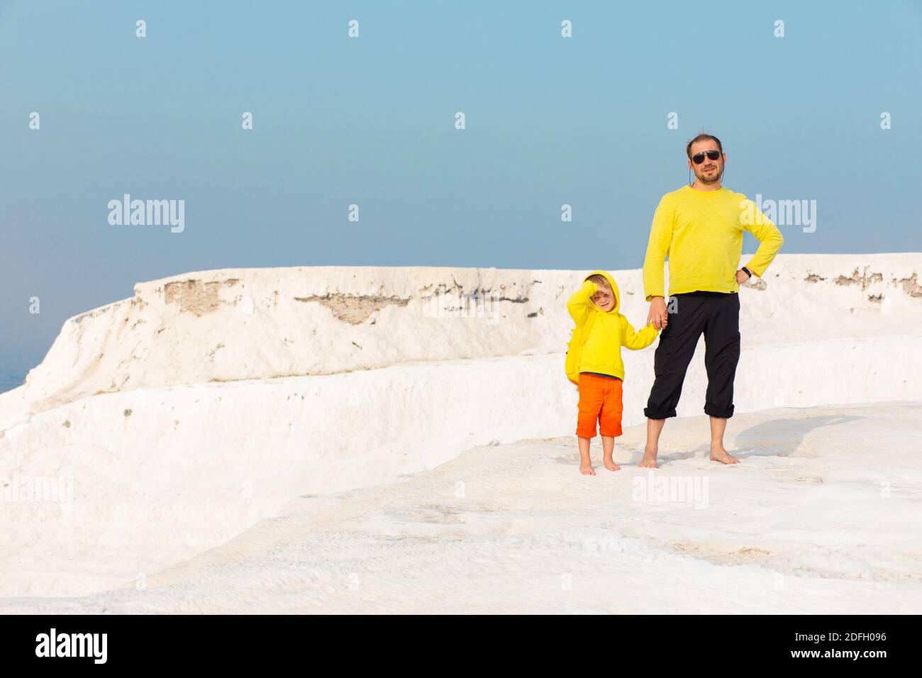 Famille, enfant fils et père en chandail jaune vif se tiennent au sommet de la montagne blanche Travertine Pamukkale en Turquie. Concept de mode de vie de voyage avec Banque D'Images