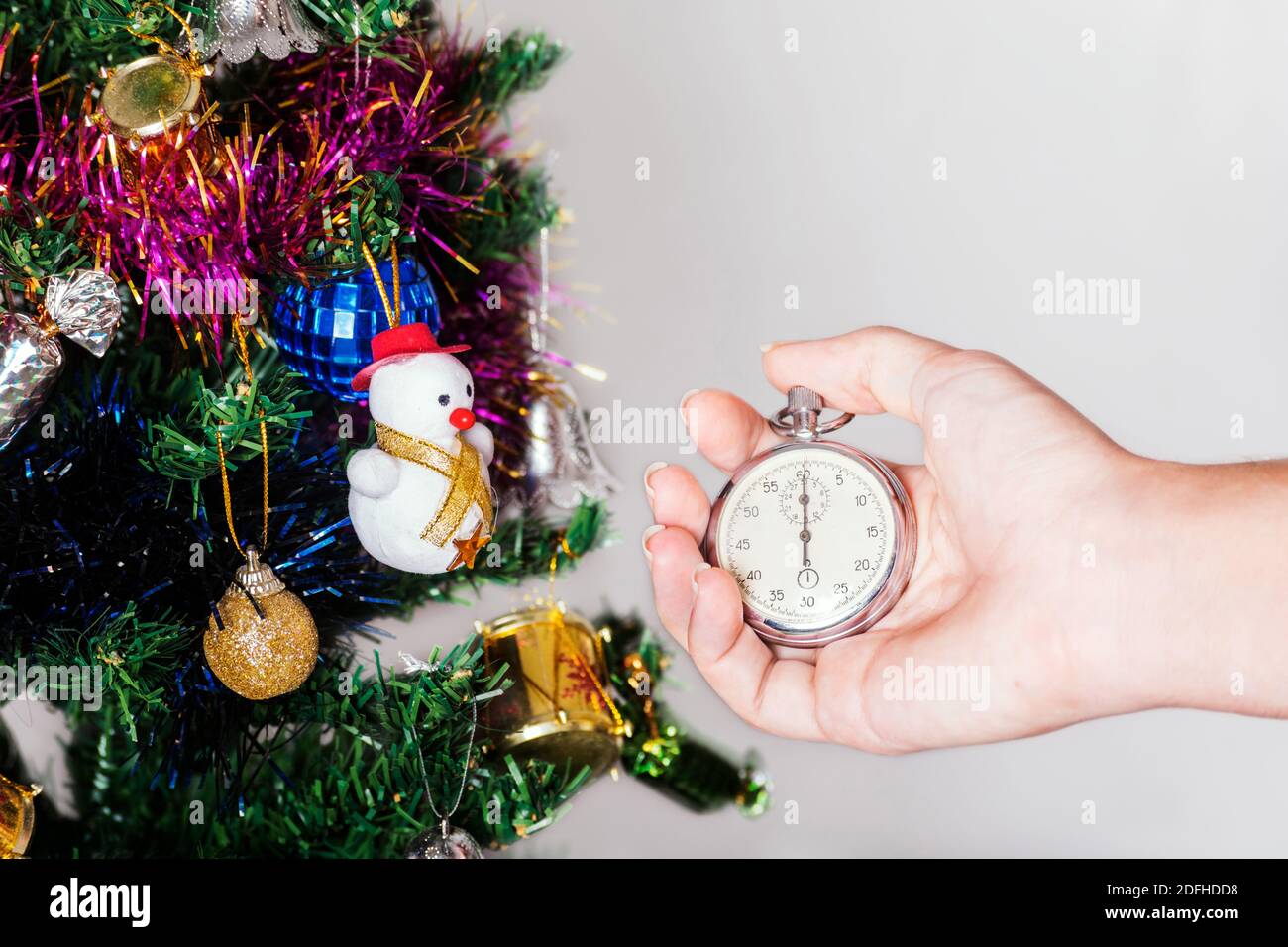 Une main caucasienne tenant un chronomètre à côté de branches décorées d'un arbre de noël Banque D'Images