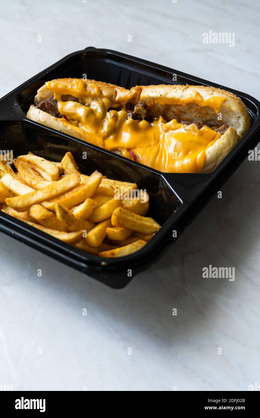 Retirez le sandwich au steak au fromage Philly accompagné de fromage cheddar fondu et de pommes de terre dans un emballage contenant en plastique. Prêt à manger Banque D'Images