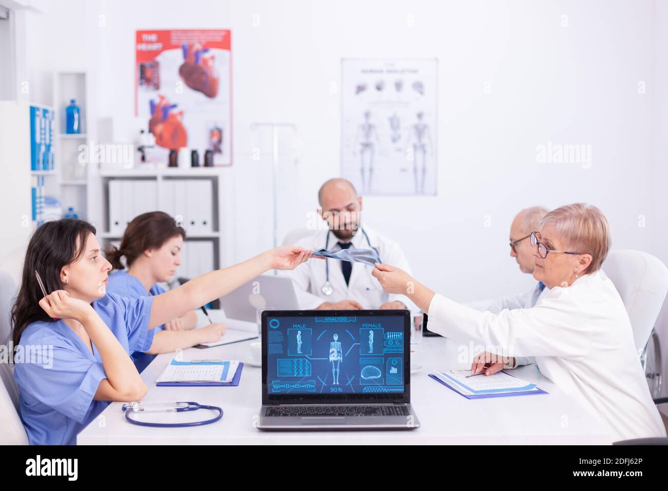 Le médecin Matude donne une radiographie à une jeune infirmière pendant la réunion du personnel dans la salle de conférence. Thérapeute expert en clinique parlant avec des collègues de la maladie, professionnel de la médecine. Banque D'Images