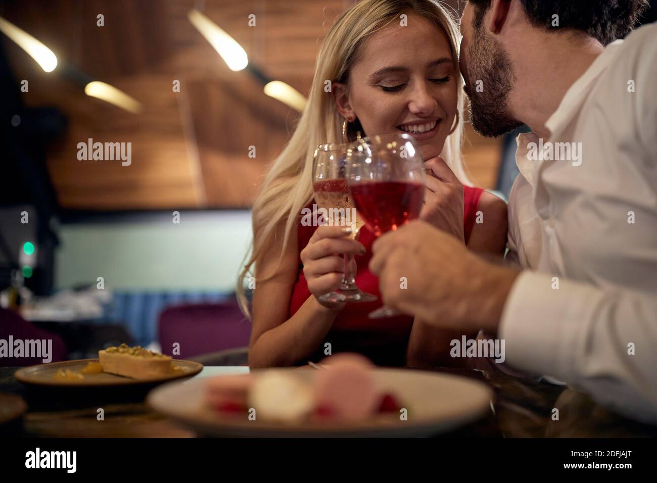 jeune homme caucasien avec une barbe chuchotant à la belle blonde au dîner romantique au restaurant Banque D'Images
