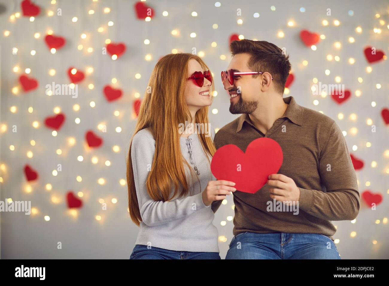 Joyeux jeune homme et femme tenant la carte de Saint-Valentin, regardant les uns les autres et souriant Banque D'Images