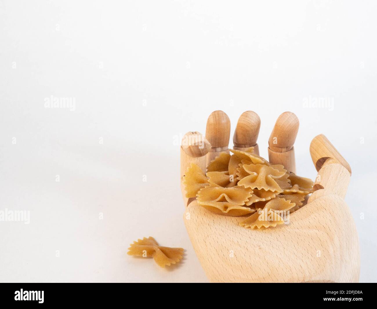 Une main en bois tenant une poignée de pâte farfalle. Concept autour de la nourriture et de la consommation. Banque D'Images