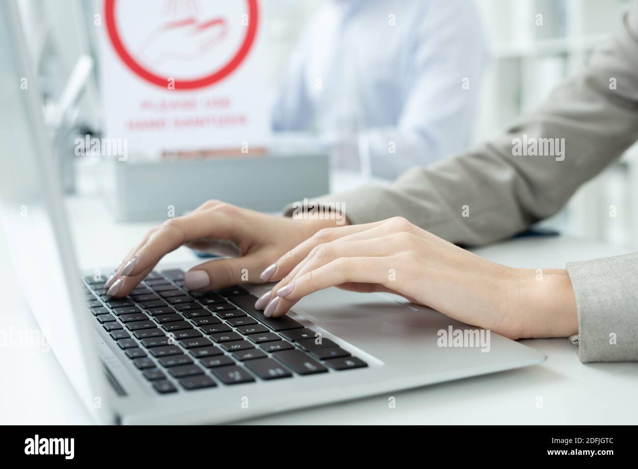 Les mains de la jeune femme d'affaires contemporaine en tenue de formal appuyant sur les touches de clavier de l'ordinateur portable pendant le réseau, assis près du bureau Banque D'Images