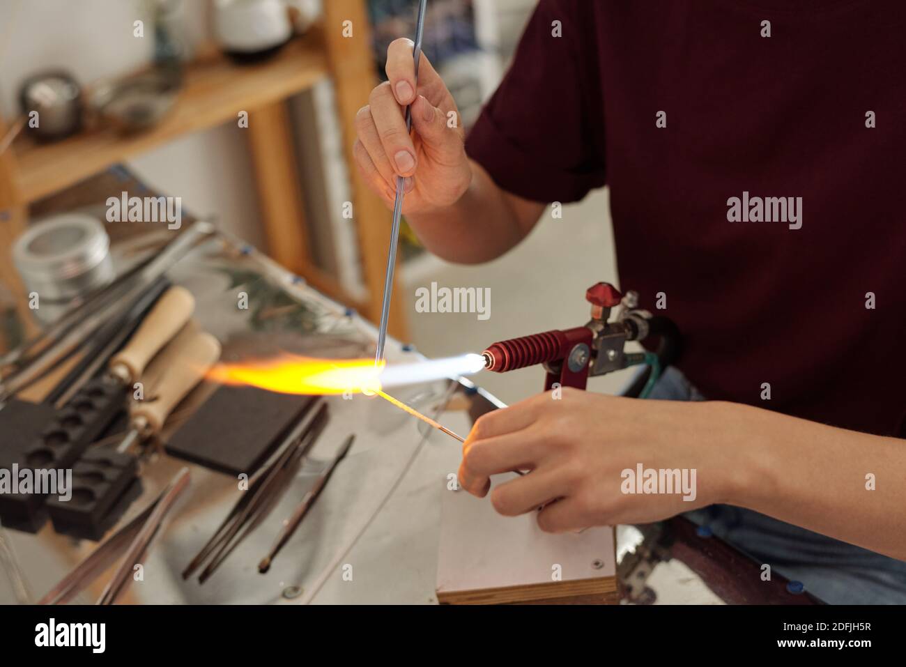 Mains de jeunes femmes artisanales contemporaines assis sur le lieu de travail et brûler la pièce au feu tout en la tenant par-dessus le brûleur atelier Banque D'Images
