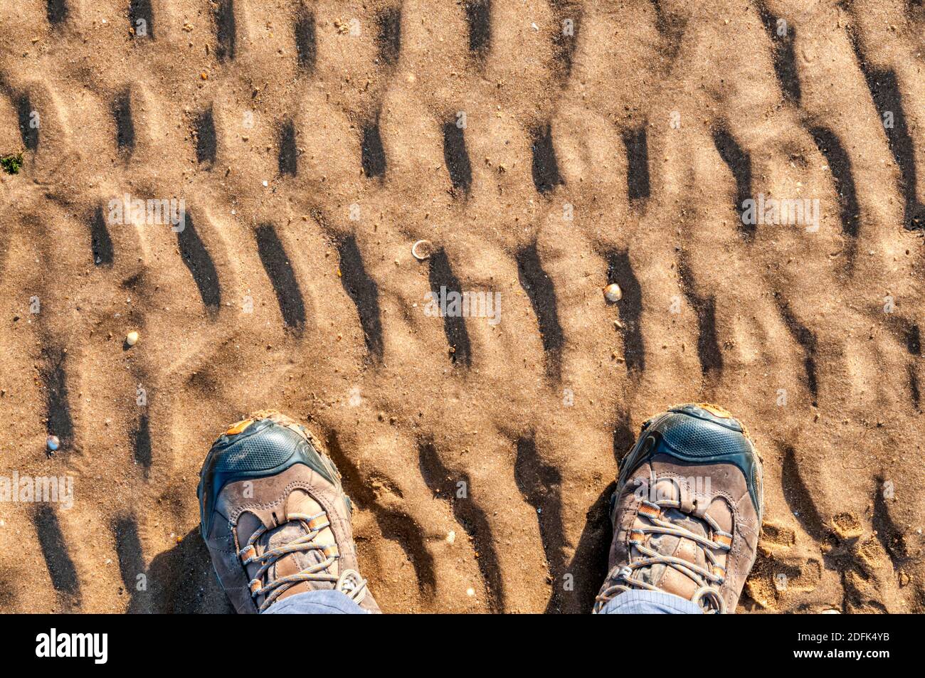 Une paire de pieds dans des bottes de marche se tenait sur le sable ondulé à la côte. Banque D'Images