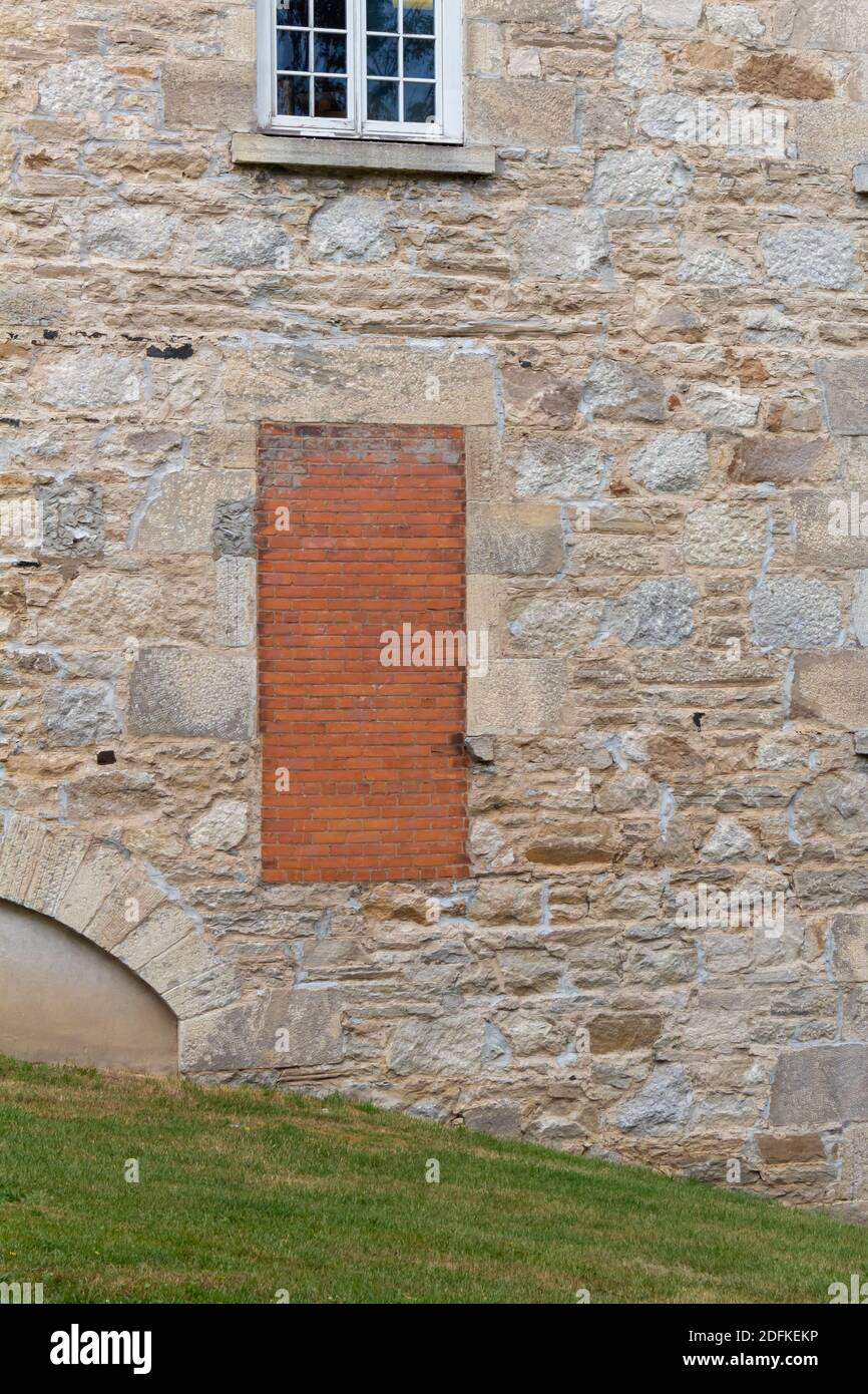Une vieille porte sur le côté d'une maison en pierre a été bricolée. Remplie de briques rouges, l'entrée apparaît à plusieurs pieds au-dessus du sol herbacé Banque D'Images
