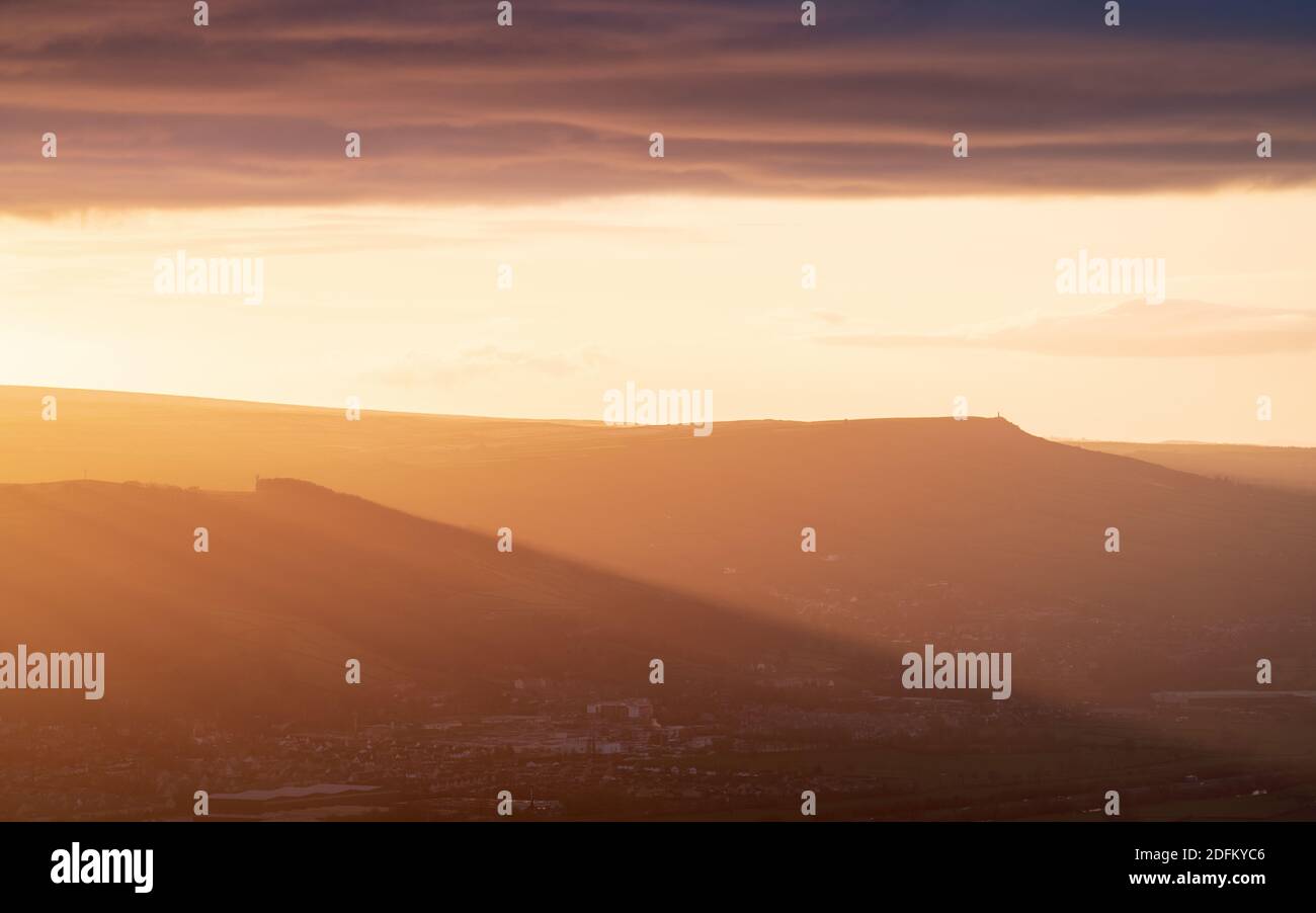 Des faisceaux de lumière spectaculaires éclairent la vallée de l'aire tandis que le soleil couchant tombe sous une rangée de nuages couveuse. Le sommet de Wainman est visible à l'horizon. Banque D'Images