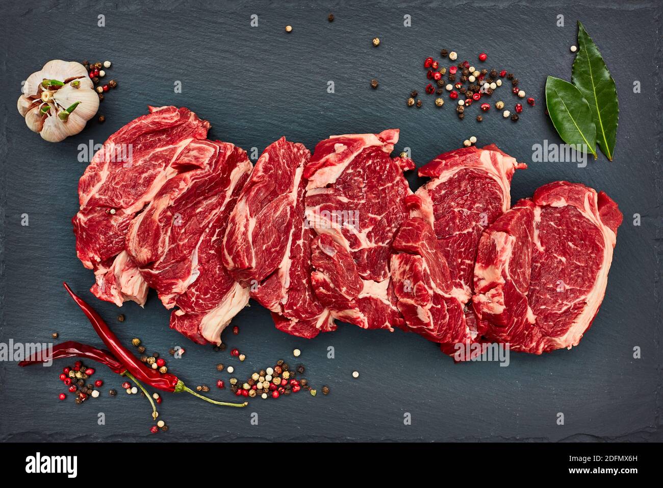 Steaks de bœuf frais crus au poivre frais sur un panneau d'ardoise noir. Espace de copie, vue de dessus. Banque D'Images