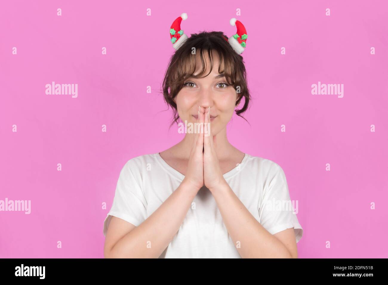 Une jeune femme avec des décorations de Noël dans ses cheveux a plié ses mains dans la prière. Isolé sur fond rose. Photo de haute qualité Banque D'Images