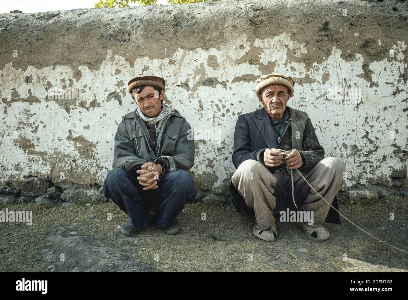 Deux hommes qui s'écrasont devant un mur d'argile, le sédentaire Wakhi, couloir de Wakhan, Saradh-e-Broghil, Afghanistan Banque D'Images