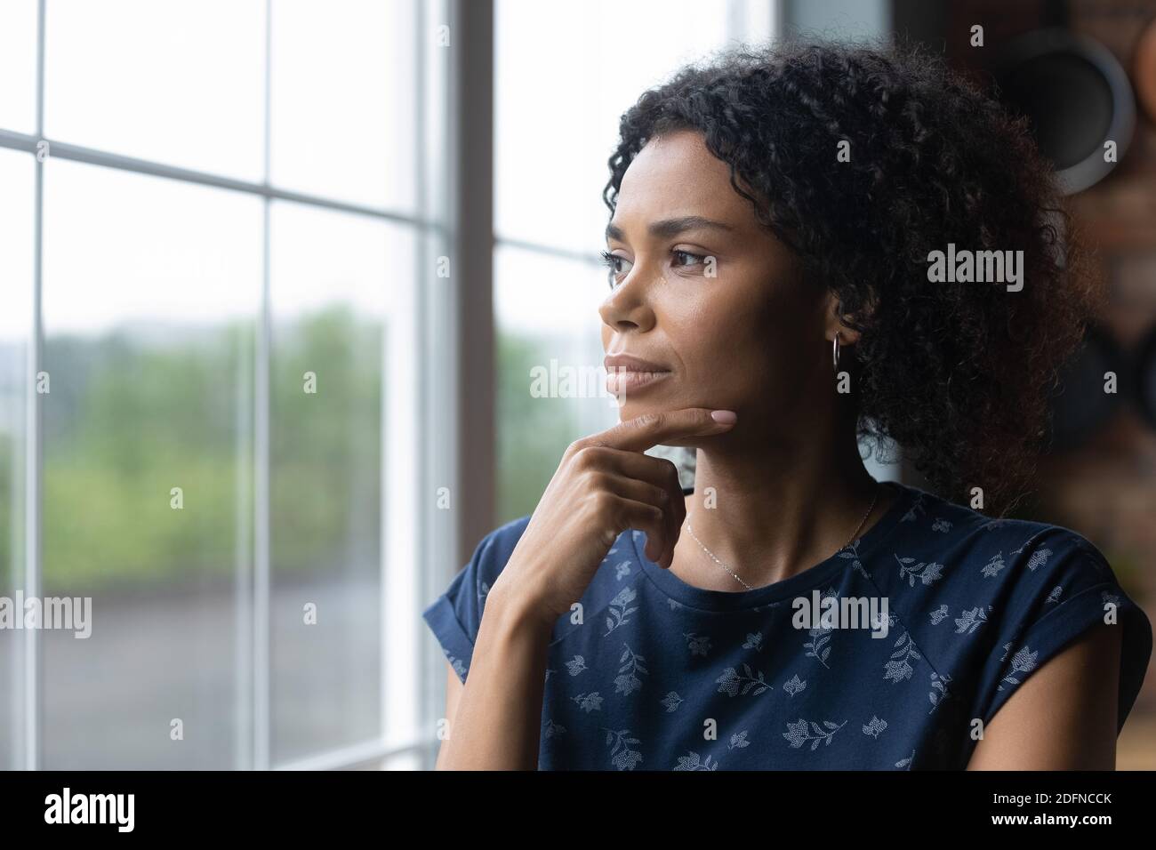 Femme afro-américaine pensive du millénaire debout près de la fenêtre. Banque D'Images