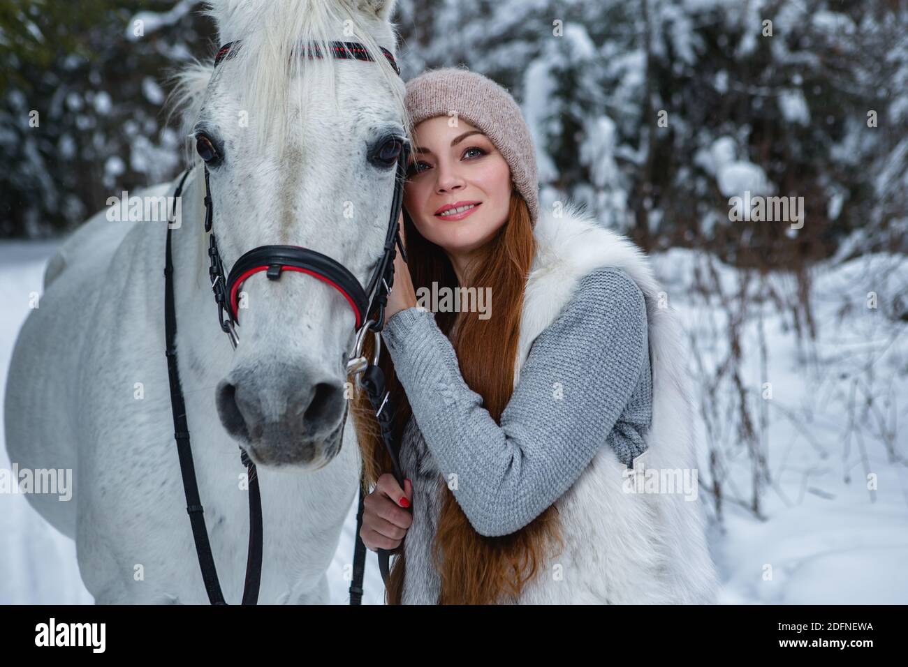 Elle tient son cheval blanc dans une forêt d'hiver Banque D'Images