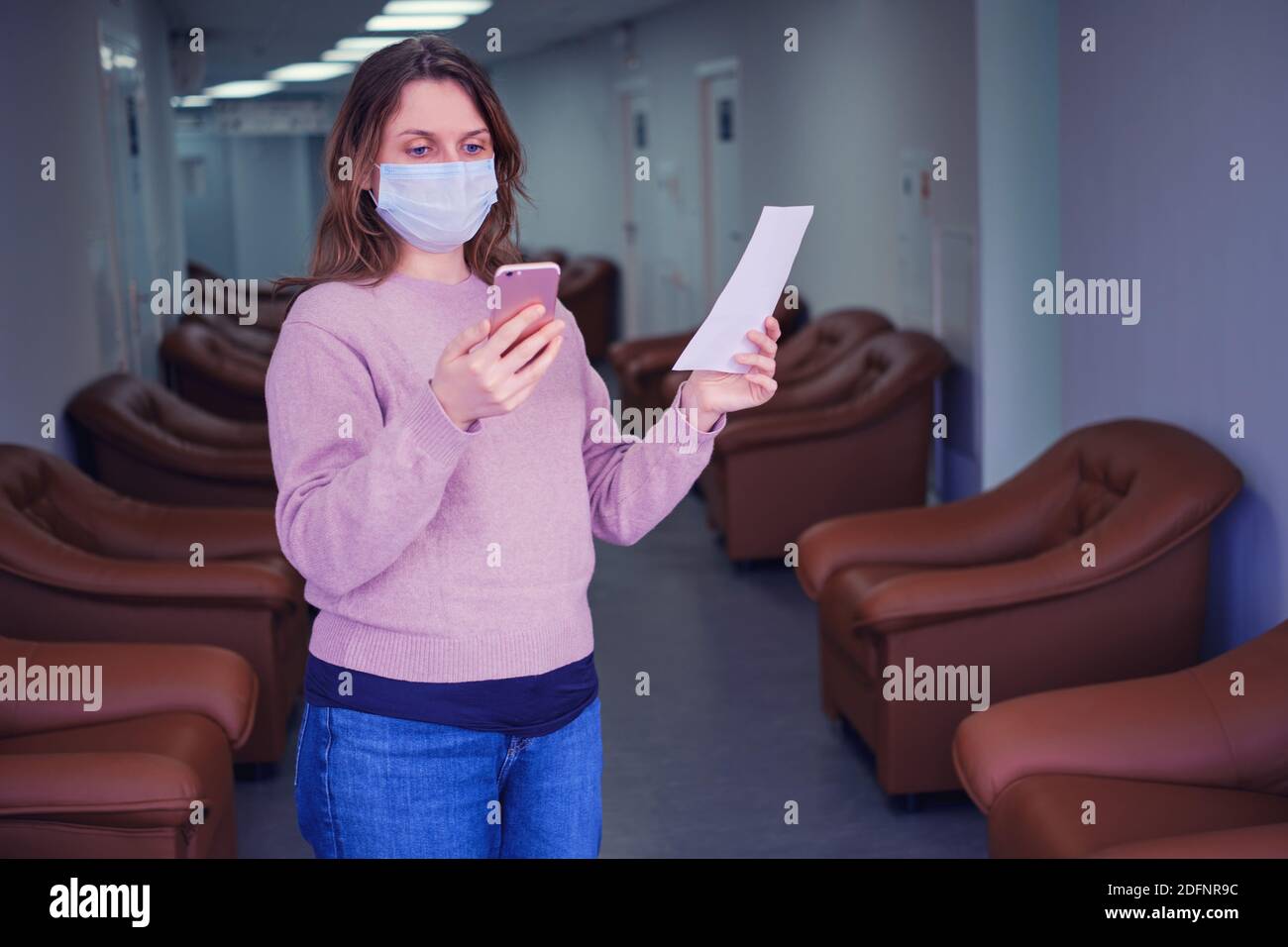 Une femme regarde son téléphone tout en se tenant dans le couloir de la clinique. Prenez rendez-vous avec un médecin en ligne et vérifiez les prescriptions sur Internet Banque D'Images