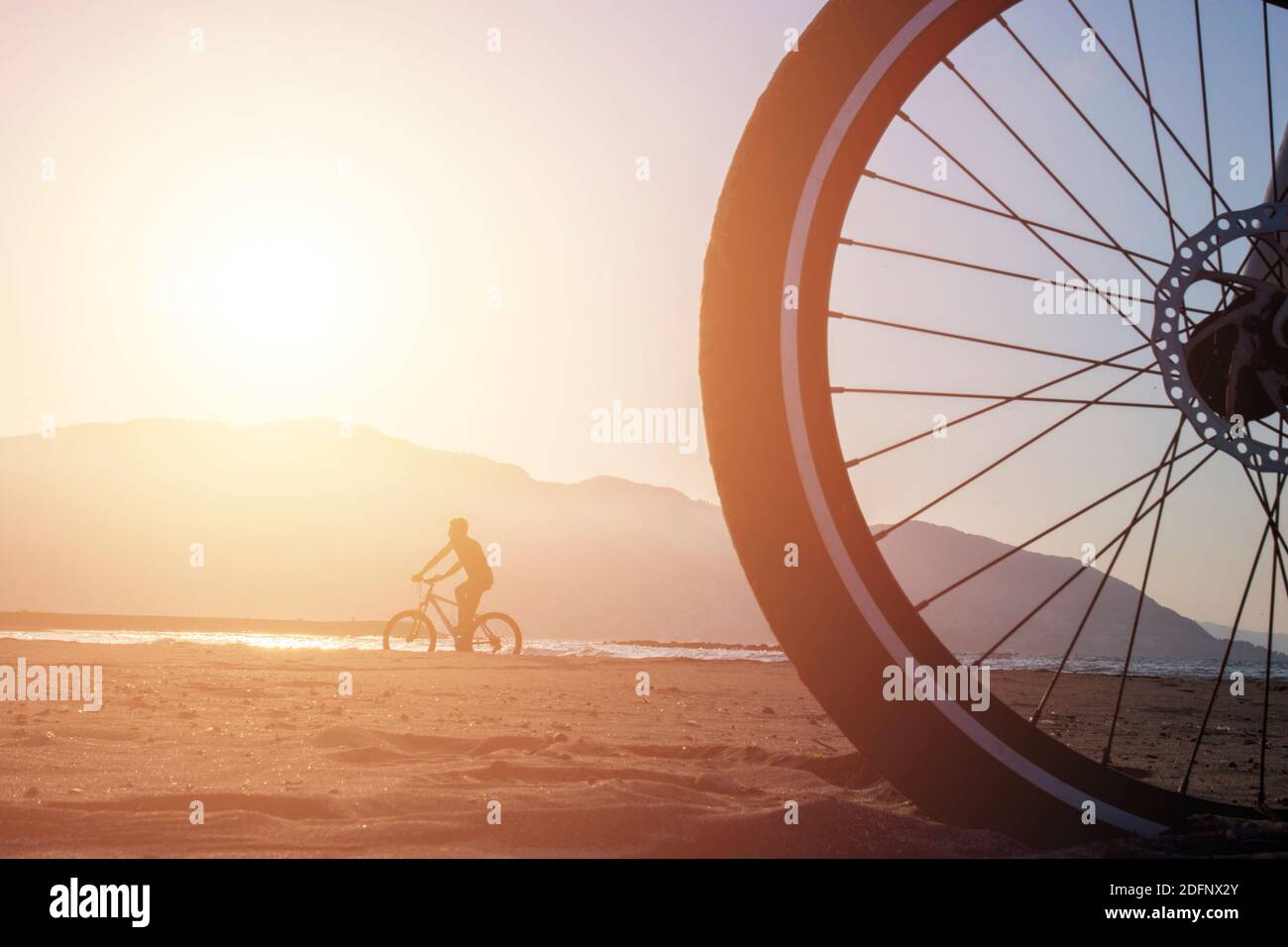 Un cycliste derrière une grande roue de vélo sur la plage. Ce sont des VTT.  Vue sur le coucher du soleil à l'arrière Photo Stock - Alamy