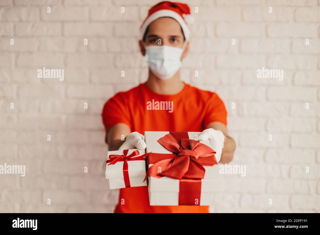 Happy man courier dans le chapeau de santa, masque médical, gants de protection donner Noël nouvel an cadeaux et sourire. Jeune homme d'accouchement dans le port de masque Banque D'Images