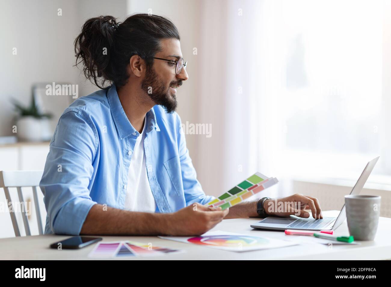 Jeune architecte d'intérieur de l'Ouest, qui tient des échantillons de nuances de couleurs et travaille sur ordinateur portable Banque D'Images