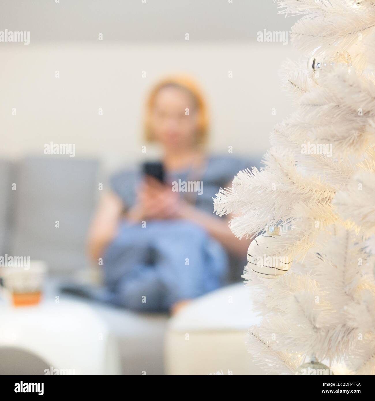 Image hors foyer d'une jeune femme gaie assise à l'intérieur canapé dans le salon de la maison utilisant les médias sociaux sur le téléphone pour le chat vidéo et rester Banque D'Images