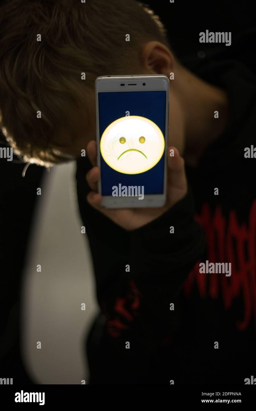 Triste emoji sur l'écran du téléphone dans les mains de un garçon Banque D'Images