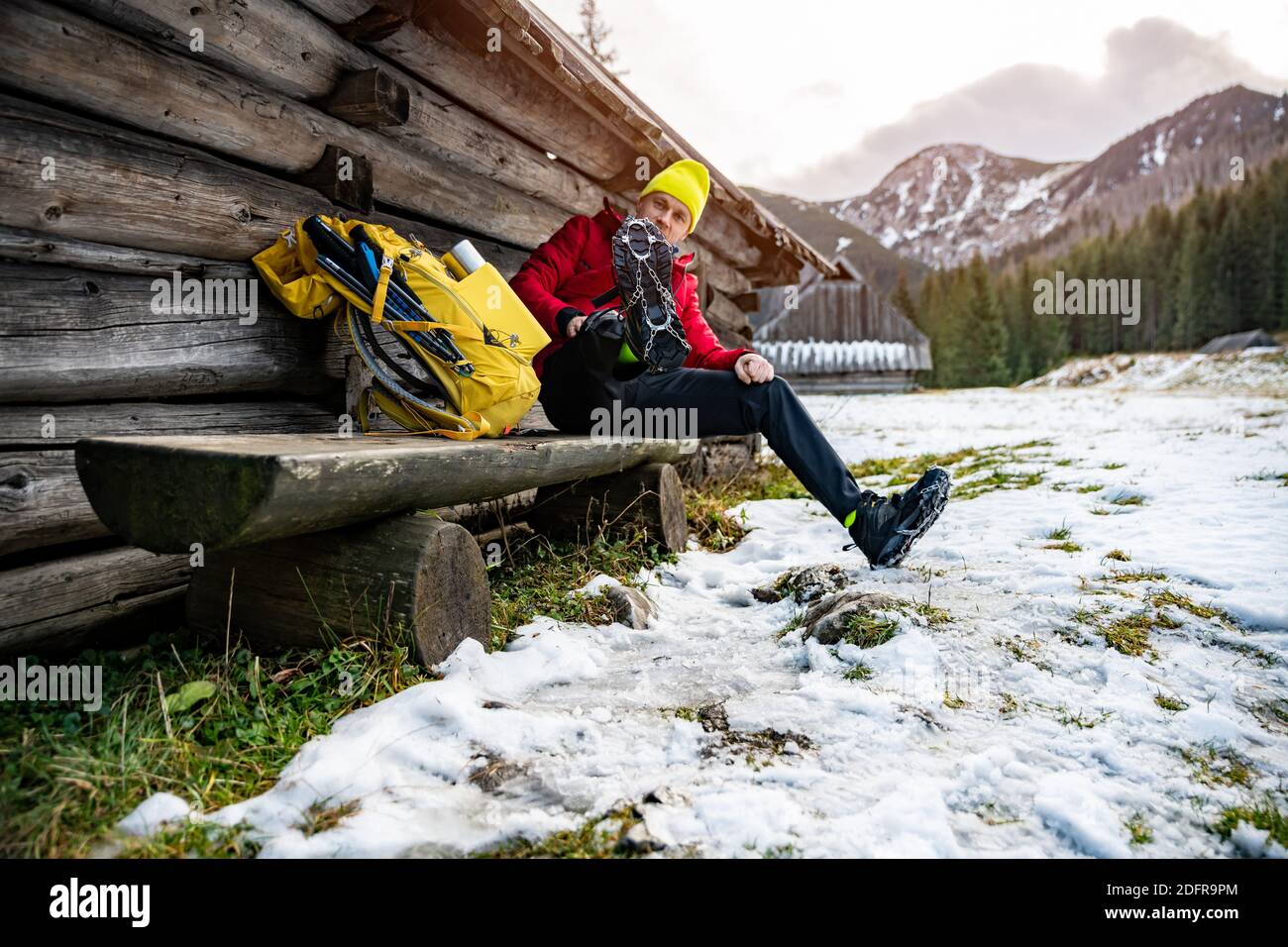 Un touriste dans une casquette jaune et une veste de duvet rouge mis sur des crampons pour les chaussures. Banque D'Images