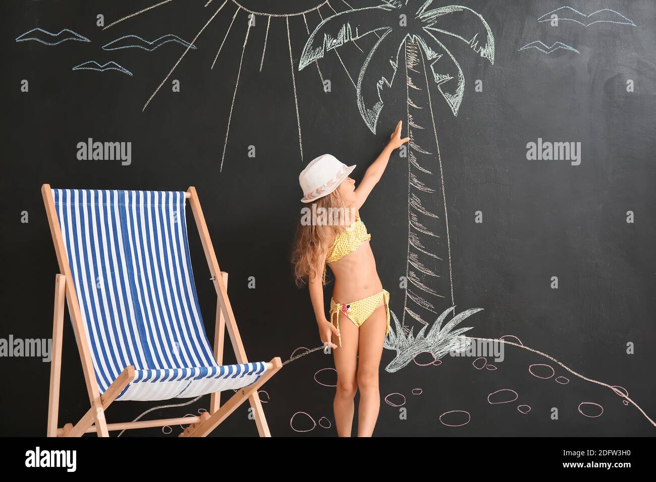 Jolie petite fille en maillot de bain près du mur noir avec dessin paume Banque D'Images