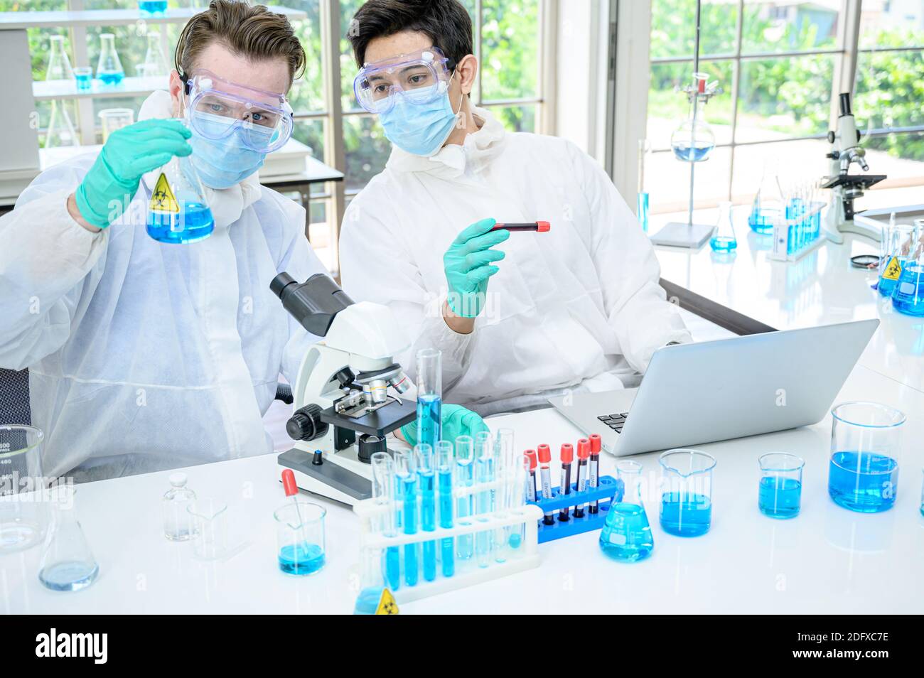 Couple scientifique mâle portant une combinaison de protection travaillant avec de nombreux équipements de laboratoire et ordinateur portable pour la recherche de vaccins en laboratoire. Traitement médical Banque D'Images