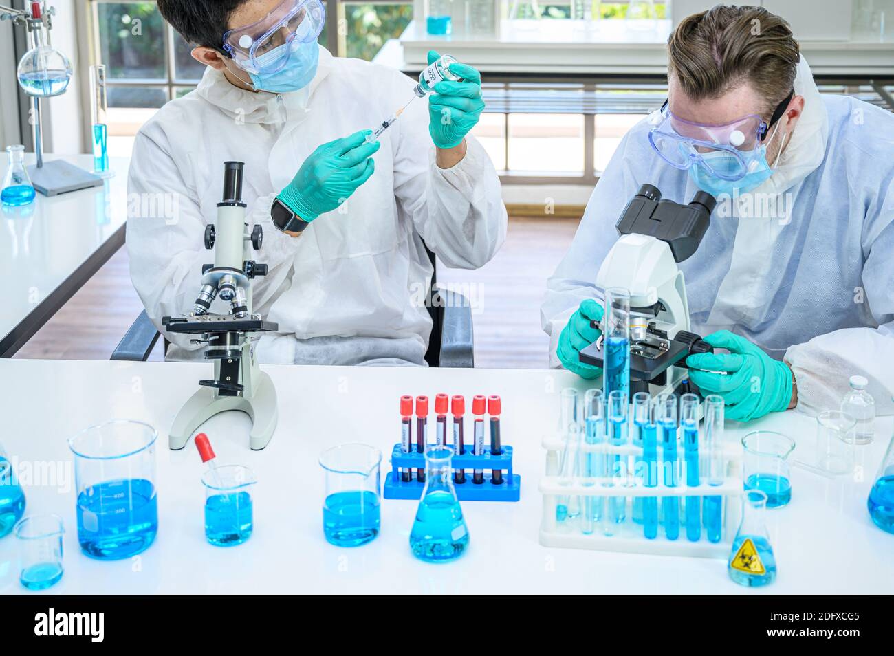 Couple de scientifiques mâles portant une combinaison de protection travaillant avec le microscope et de nombreux équipements de laboratoire pour la recherche du vaccin contre le coronavirus en laboratoire. Virus réf Banque D'Images