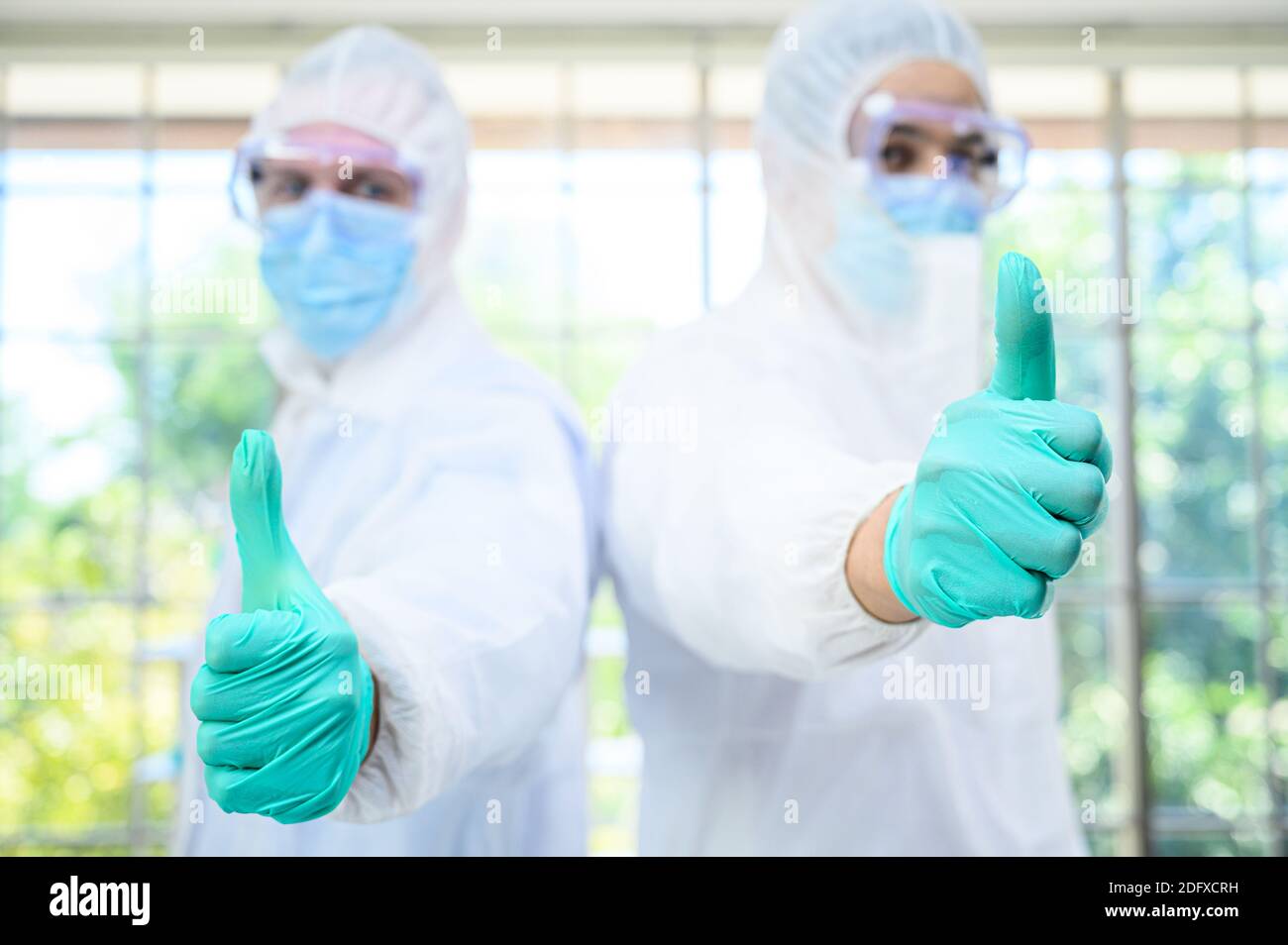 Couple de scientifiques mâles portant une combinaison de protection montrant le pouce vers le haut et se tenir sur le fond en verre au laboratoire. Portrait du scientifique Banque D'Images