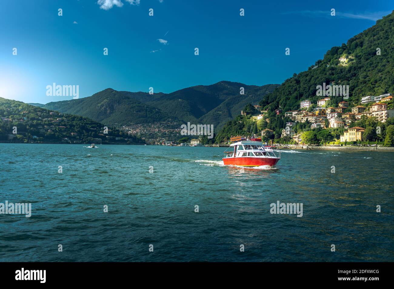 Lac de Côme dans la ville de Côme, Lombardie, Italie. Paysage pittoresque avec montagnes et bateau rouge naviguant sur l'eau Banque D'Images