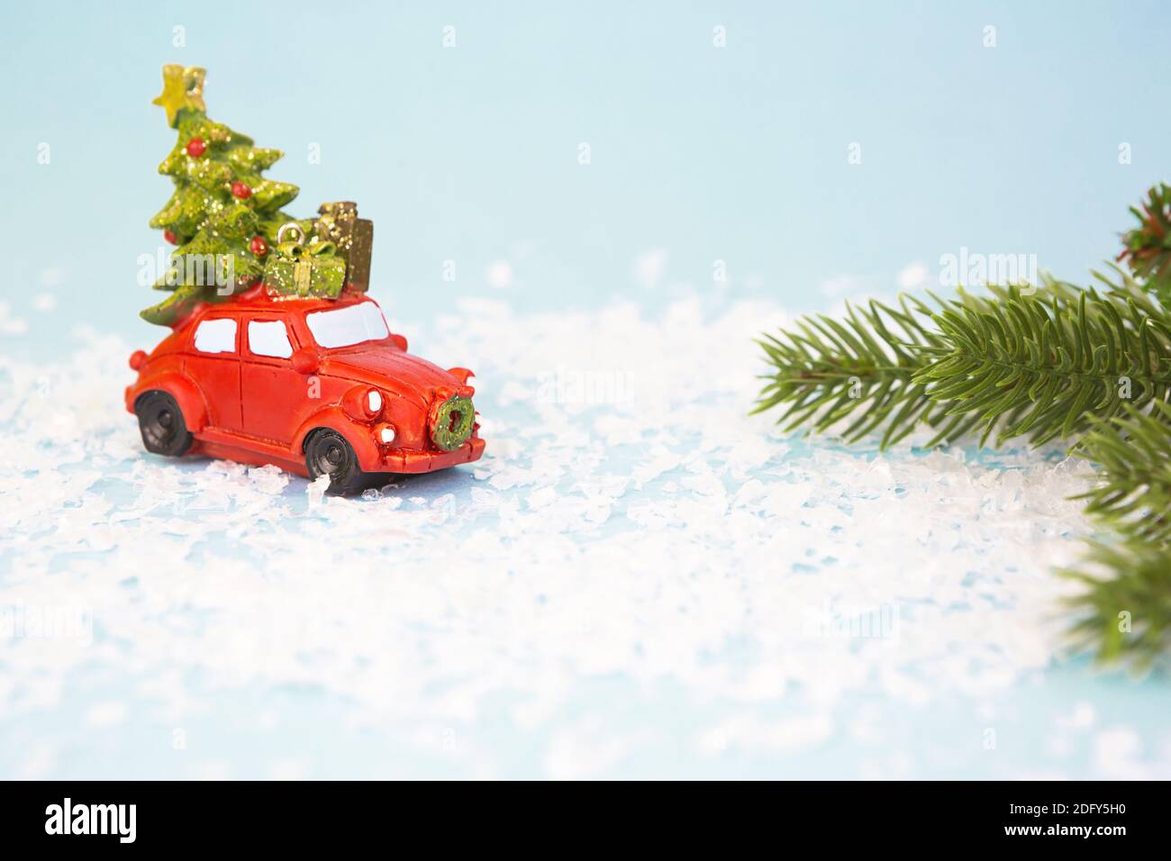 Décoration de Noël - une voiture rétro rouge sur neige artificielle porte un arbre de Noël avec des boîtes-cadeaux sur le toit. Jouet avec paillettes sur fond bleu, spac Banque D'Images