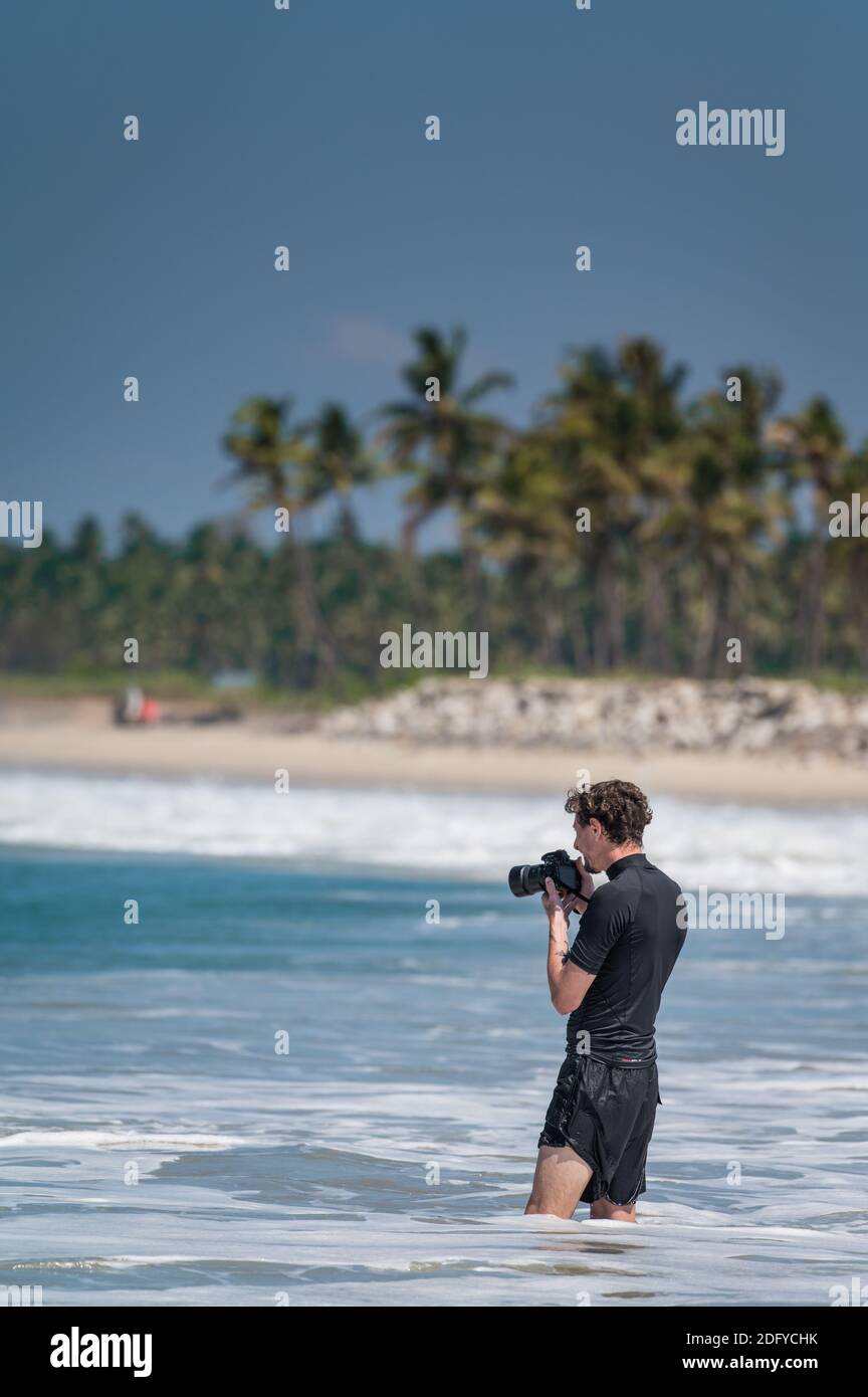VARKALA, INDE - 14 mars 2020 : étranger avec sa caméra capturant les surfeurs dans la mer Banque D'Images