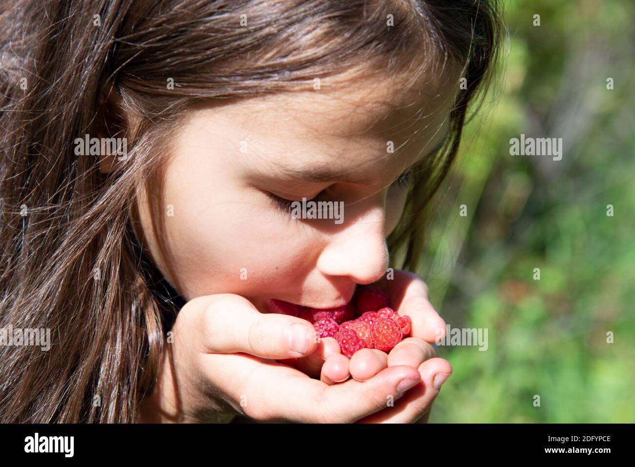 Une fille mange des framboises sauvages des paumes de ses mains en gros plan. Le visage de fille avec des baies sur un fond vert.le concept de la santé naturelle FO Banque D'Images
