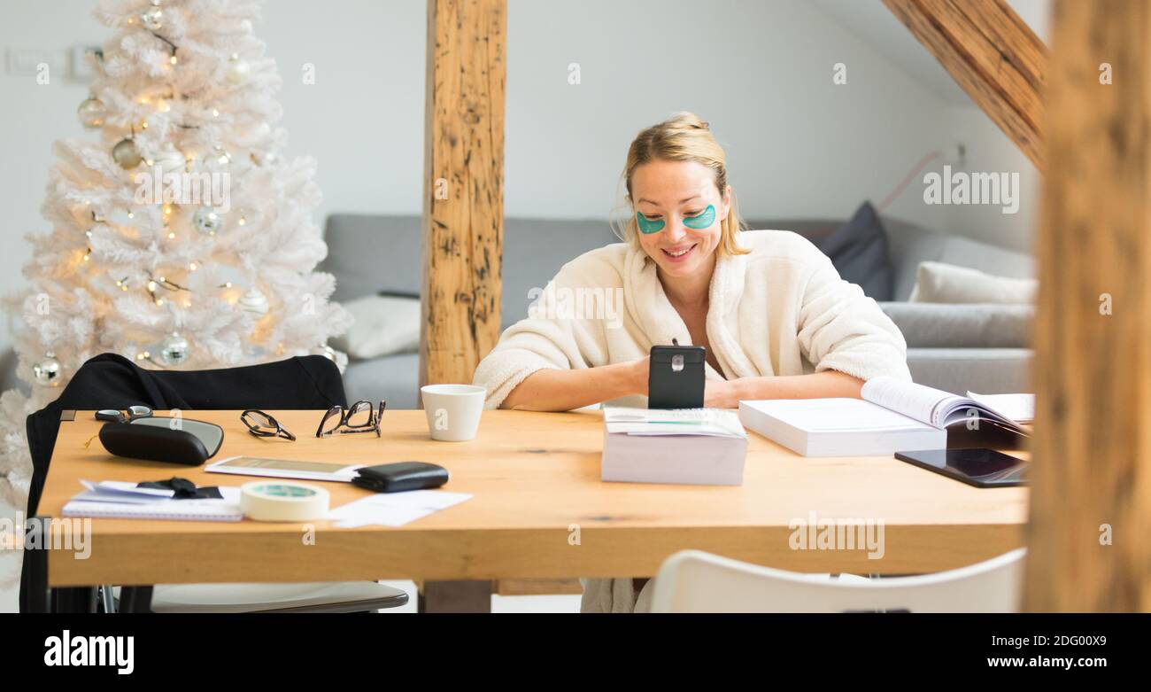 Jeune femme d'affaires portant un peignoir chaleureux et des timbres cosmétiques pour les yeux Travailler à distance de la maison pendant les fêtes d'hiver en 2020 virus corona Banque D'Images