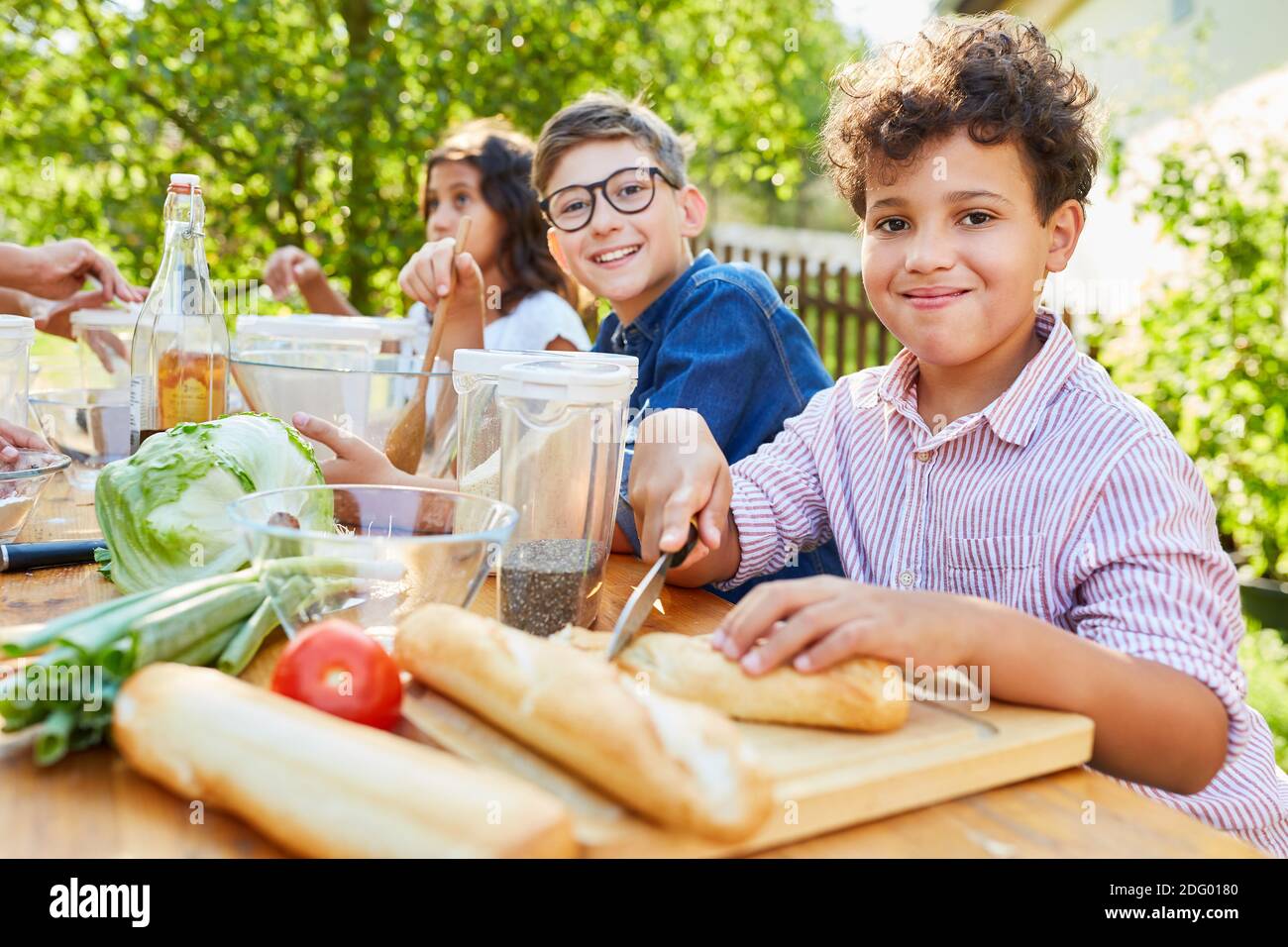 Garçon avec des amis en cours de cuisine lors des coupes de camp d'été pain de baguette pour une salade Banque D'Images