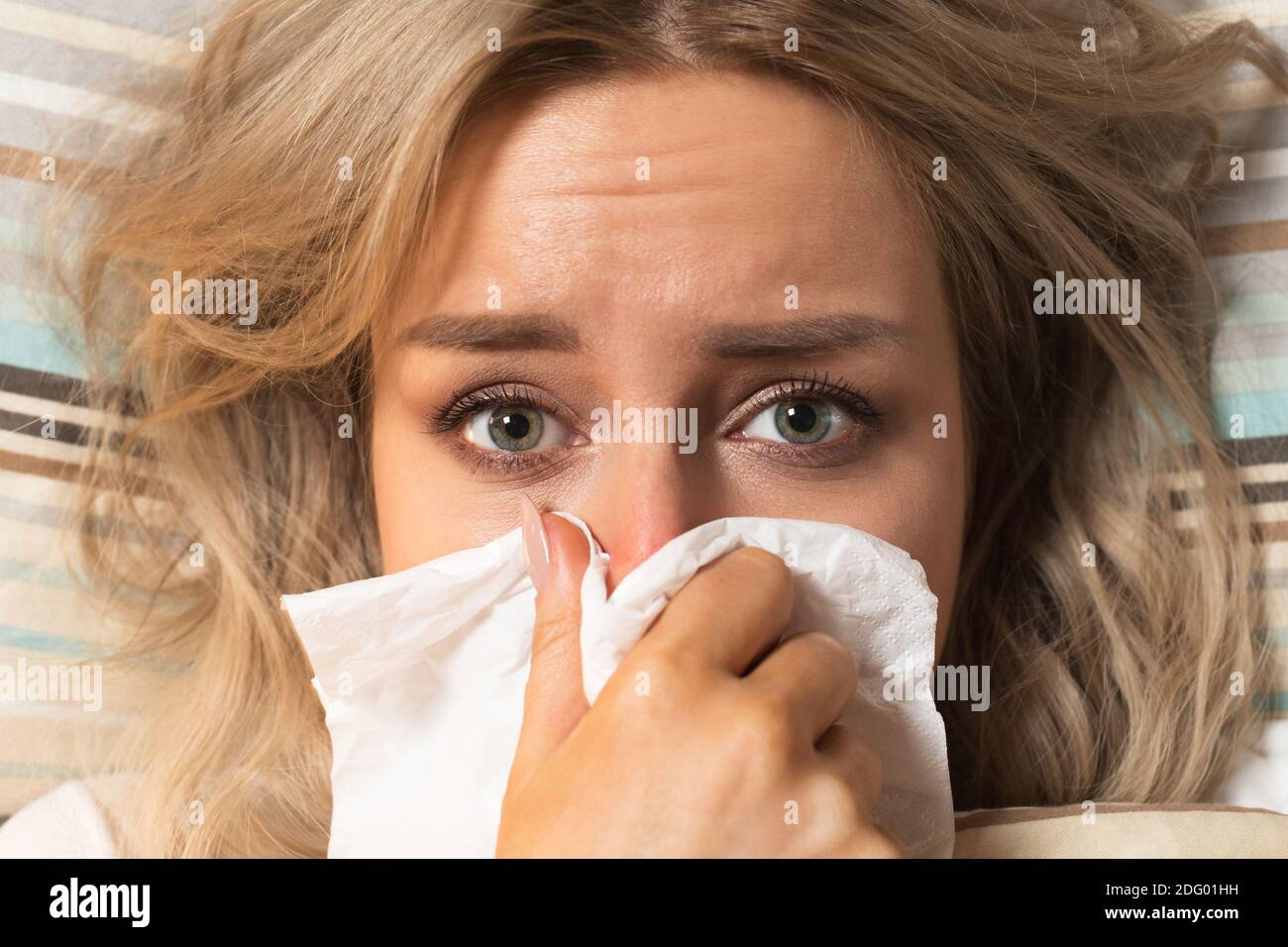Jeune femme européenne bouleversée et malade avec une serviette en papier soufflant le nez, couché sur le lit, regardant la caméra, vue de dessus. Rhinite, saison de la grippe. Banque D'Images