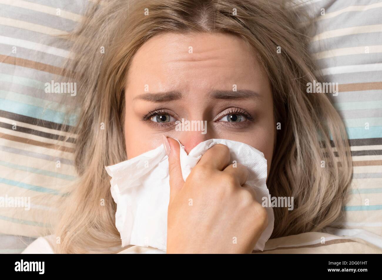 Femme malade avec serviette en papier soufflant nez, allongé sur le lit, regardant l'appareil photo, vue de dessus. Rhinite, saison de la grippe. Banque D'Images