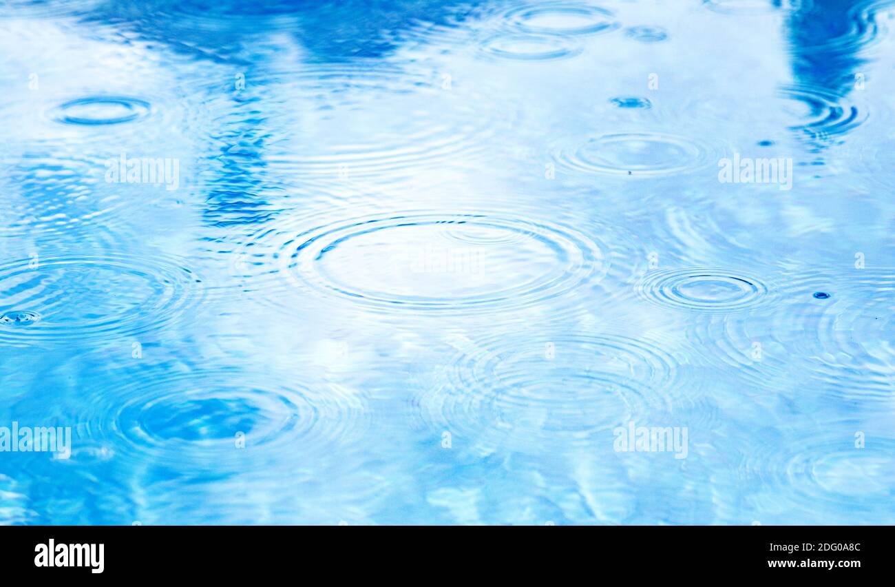 Taches les cercles sur l'eau de la pluie. Gouttes de pluie sur la surface de l'eau bleu de la piscine. Texture de l'eau bleue comme arrière-plan. Banque D'Images