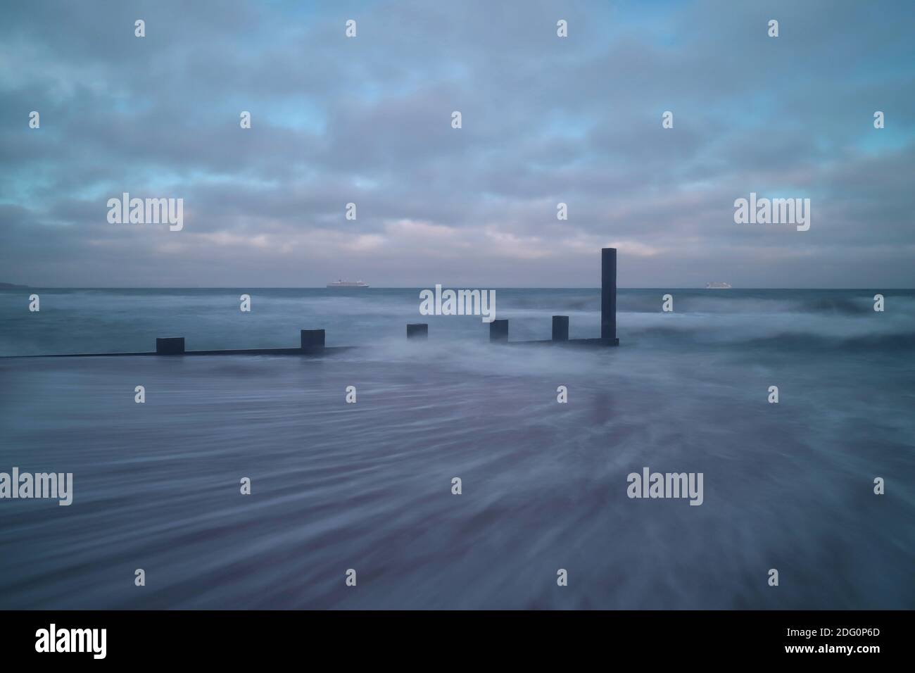 Les vagues laissent des sentiers sur le sable alors qu'elles s'éloignent de la rive. Pendant ce temps, la mer s'écrase sur le bois abîmé de l'aine de défense de la mer provocante Banque D'Images