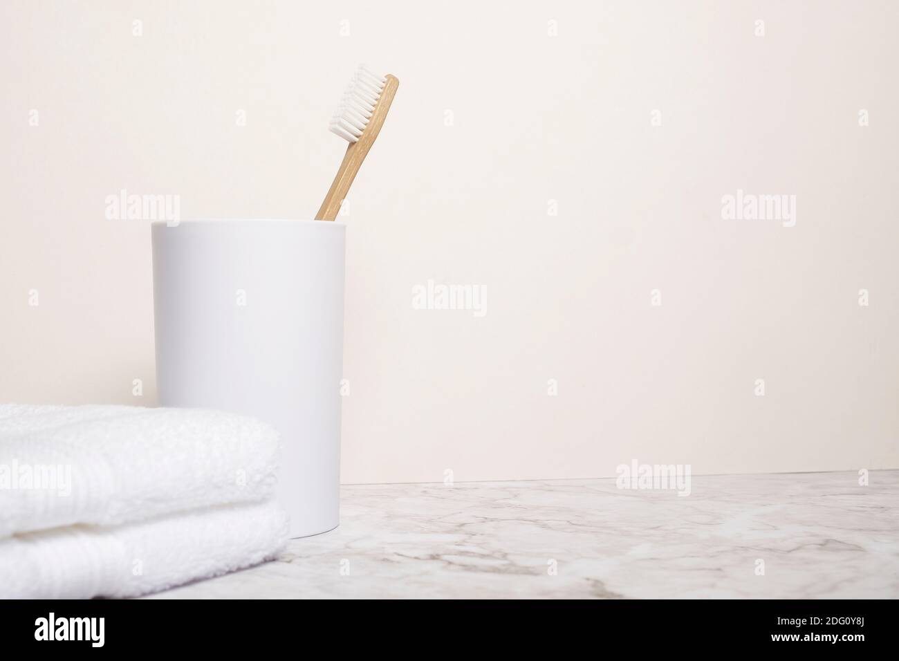 Brosse à dents en bambou en bois naturel dans une tasse blanche à un chiffon blanc sur une surface en marbre avec copie espace et espace pour le texte Banque D'Images