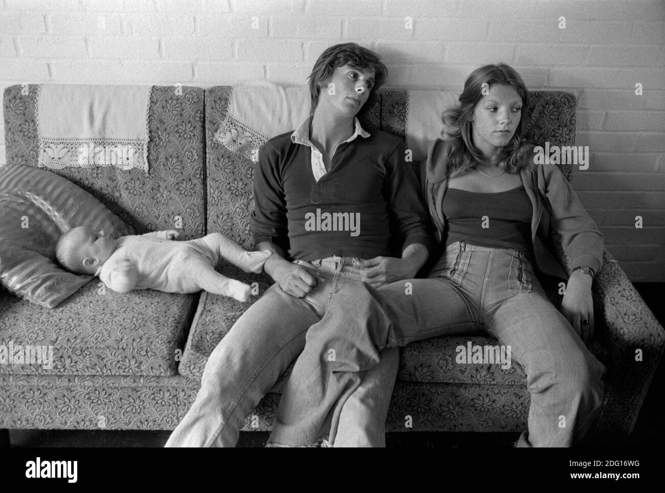 1970s jeune couple de classe moyenne à la mode en jeans, vêtements décontractés, dans les jambes d'amour touchant, se détendre, dans une maison d'amis.c'est pas leur bébé. 1977 Milton Keynes, Buckinghamshire Royaume-Uni HOMER SYKES Banque D'Images