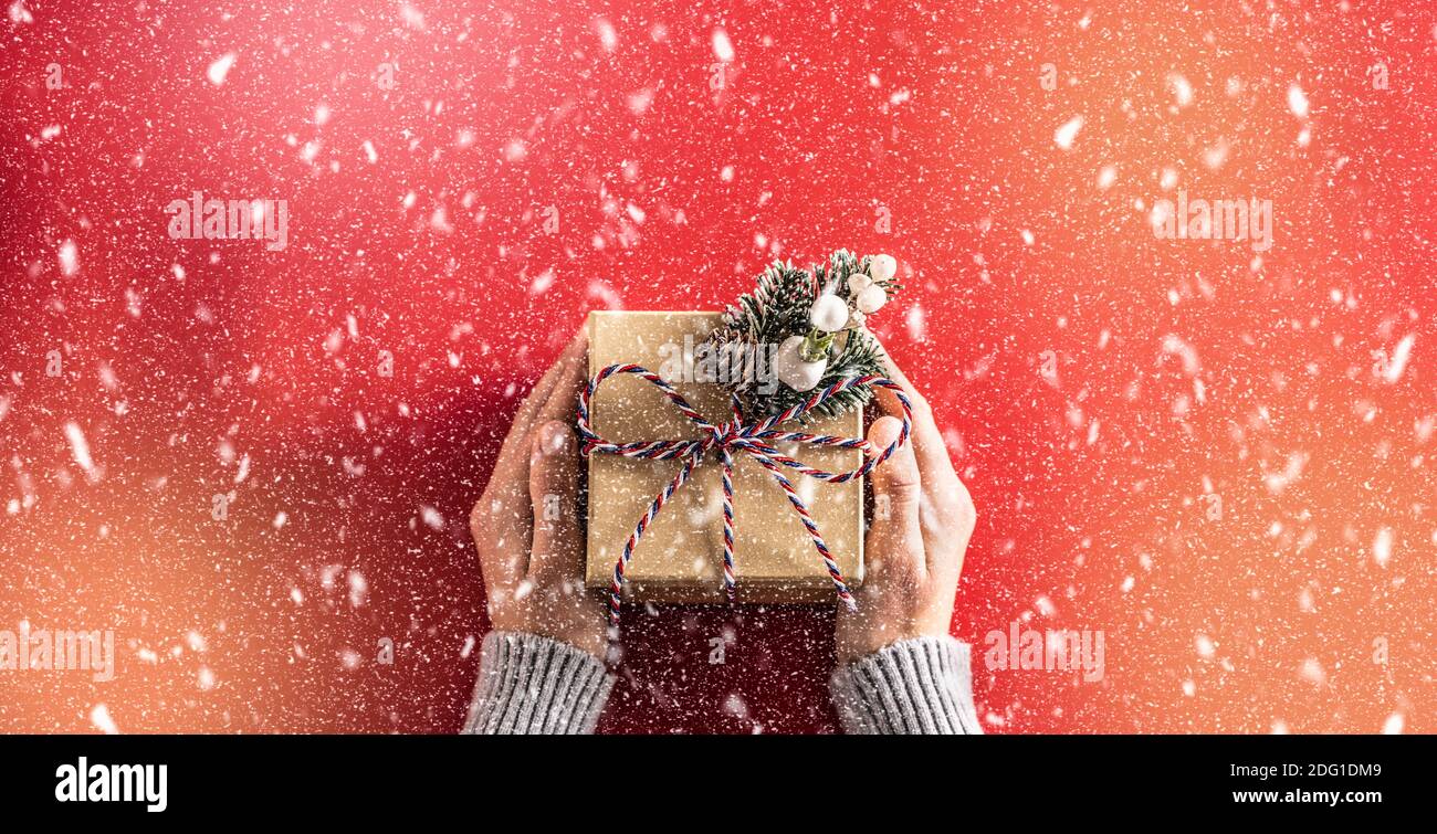 Boîte-cadeau en papier avec noeud dans les mains des femmes sur fond rouge en chute de neige abstraite. Banque D'Images