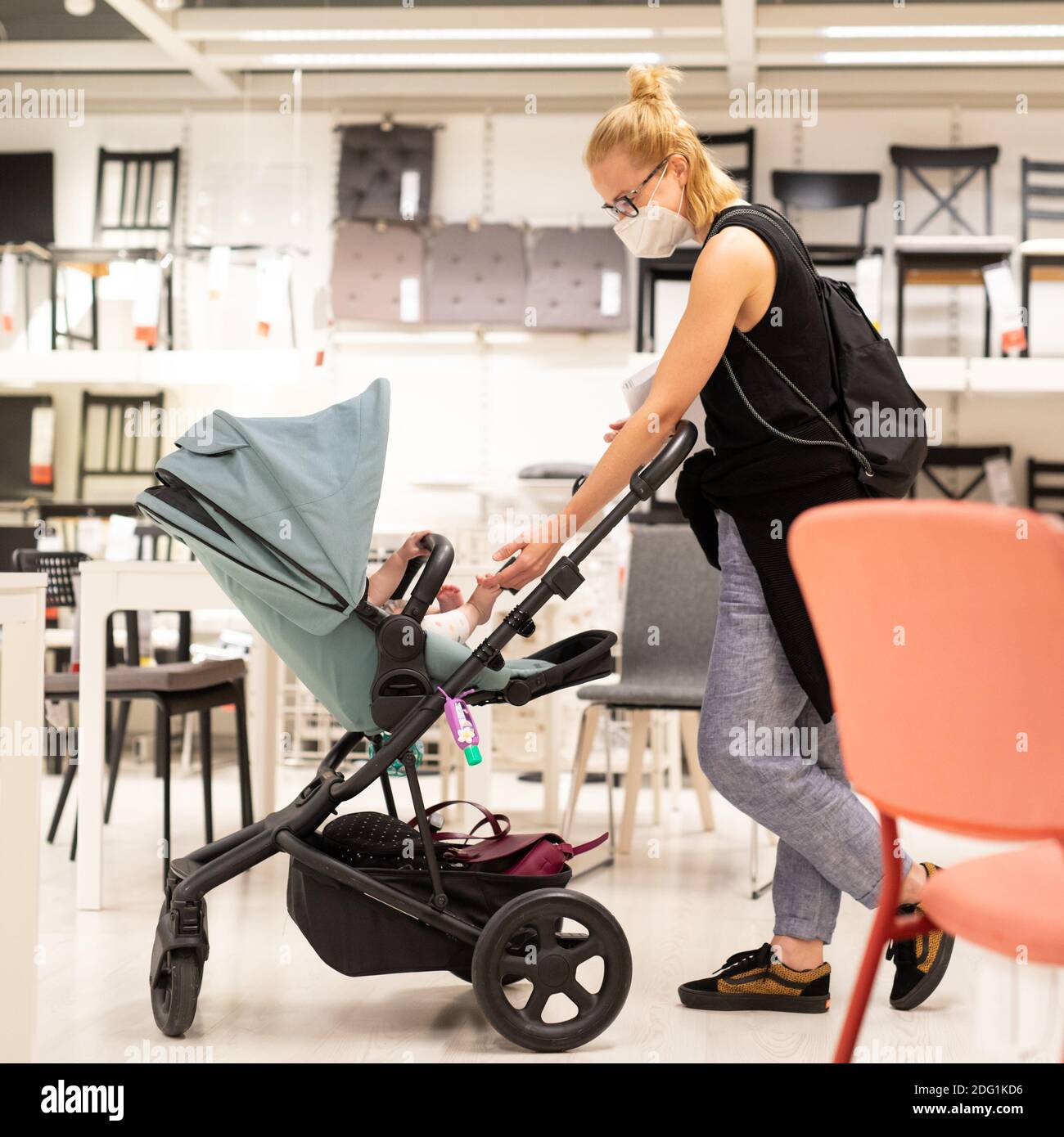 Jeune maman avec nouveau-né dans le magasin de poussettes au détail de meubles et maison accessoires magasin portant un masque médical de protection pour le visage à empêcher l'épandage Banque D'Images