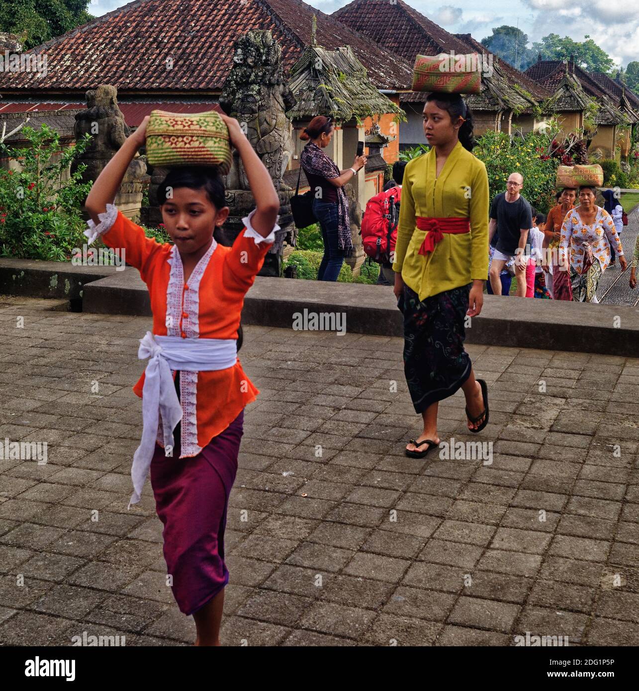 Les femmes indonésiennes en vêtements traditionnels portant des paniers sur leur tête au village modèle traditionnel de Penglipuran à Bali avec de nombreux touristes visibles Banque D'Images