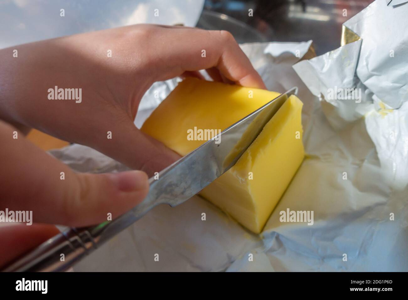 Un enfant utilise un couteau de table pour trancher un bloc de beurre. Banque D'Images