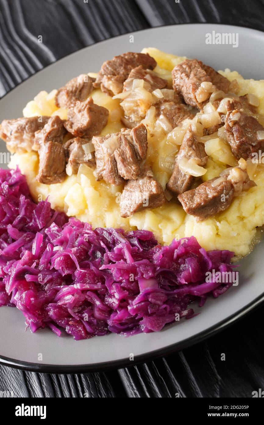 Ragoût de bœuf et d'oignon Hachee servi avec une purée de pommes de terre, le chou rouge braisé dans l'assiette sur la table. Vertical Banque D'Images