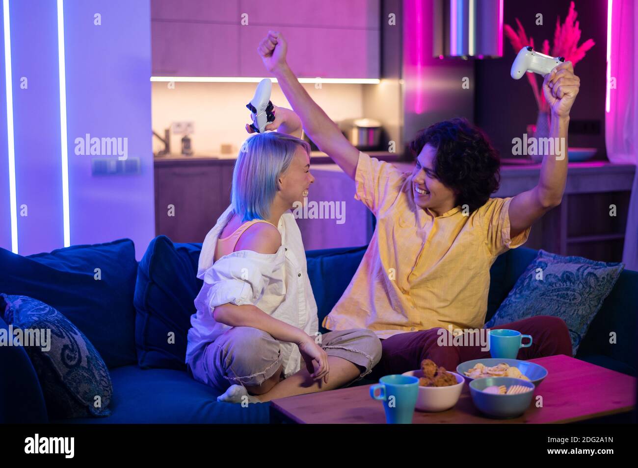 Joyeux petit ami et petite amie jouant à des jeux vidéo et tenant des joysticks à la maison. Couple du millénaire qui profite du jeu tout en étant assis sur un canapé et en dépensant Banque D'Images