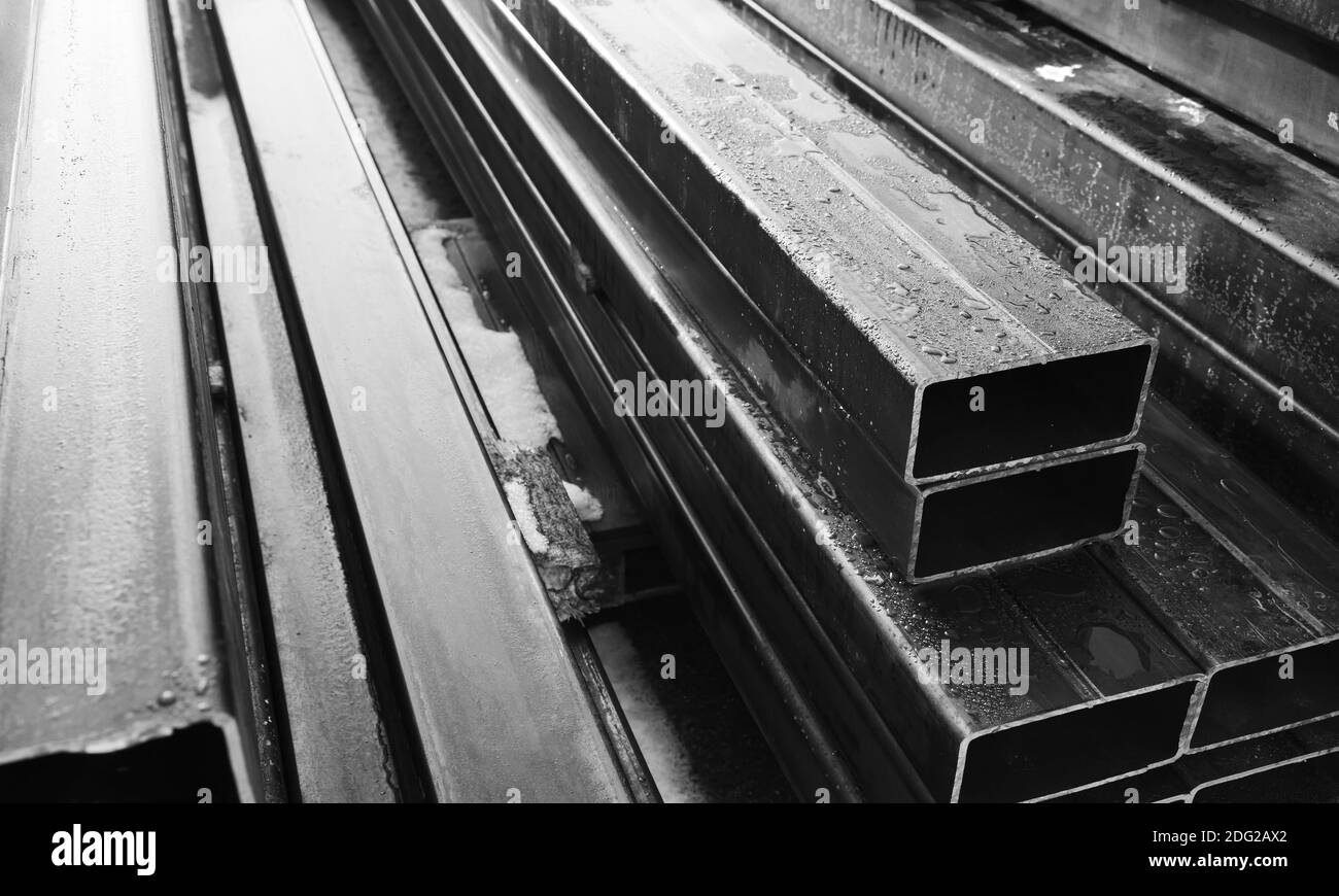 Pile de produits métalliques laminés, tuyaux en acier gris avec section transversale rectangulaire, photo en gros plan noir et blanc avec mise au point douce sélective Banque D'Images