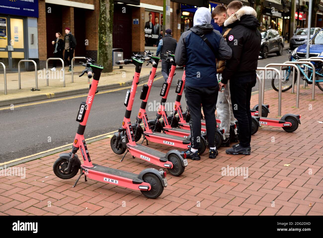 Trois jeunes hommes qui cherchent à louer des e-trottinettes électriques en utilisant l'application Au téléphone à Bristol Banque D'Images